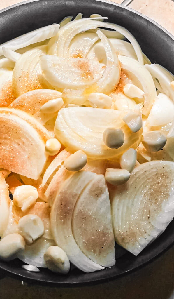 a skillet full of sliced yellow onions and garlic cloves