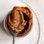an overhead shot of date caramel in a jar with a scoop of caramel on a spoon resting on the mouth of the jar