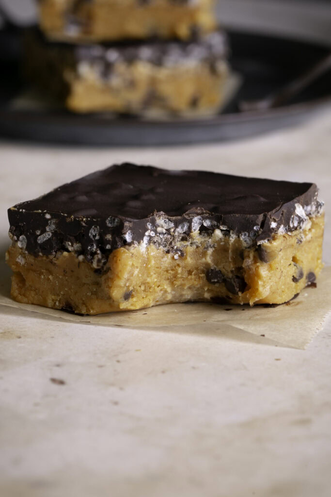 a close up of one Almond Flour Pumpkin Cookie Dough Crunch Bar on a piece of parchment paper, a bite taken out of it
