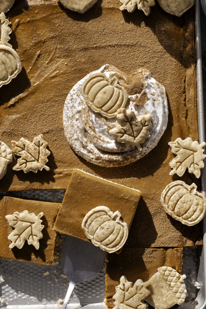 a close up of Sheet Pan Pumpkin Pie, decorated with a dollop of whipped cream and pie crust cut outs. The bottom half of the pie is sliced into squares