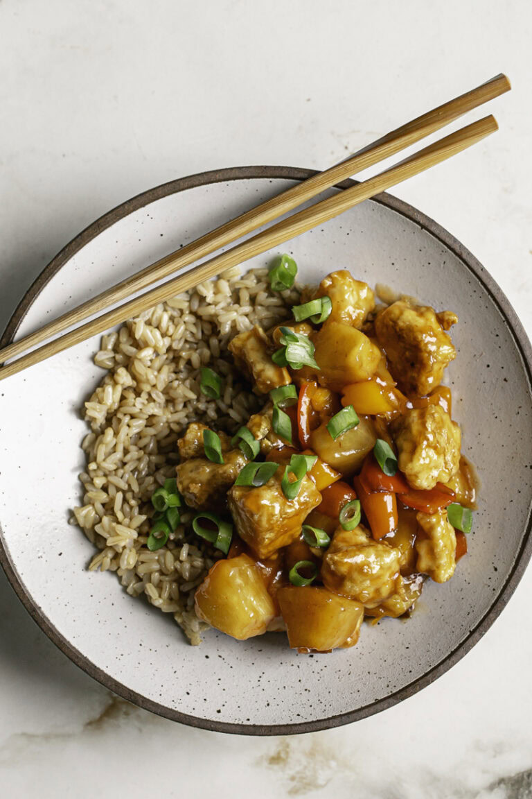 a bowl of 30 Minute Sweet & Sour Tofu garnished with fresh green onion and wooden chopsticks resting on the bowl