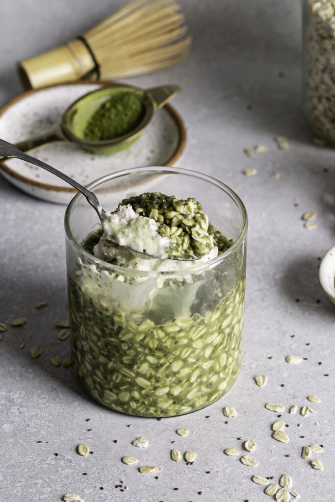 an action 3/4 shot of a glass of Oat Milk Matcha Latte Overnight Oats with a spoon scooping some overnight oats out