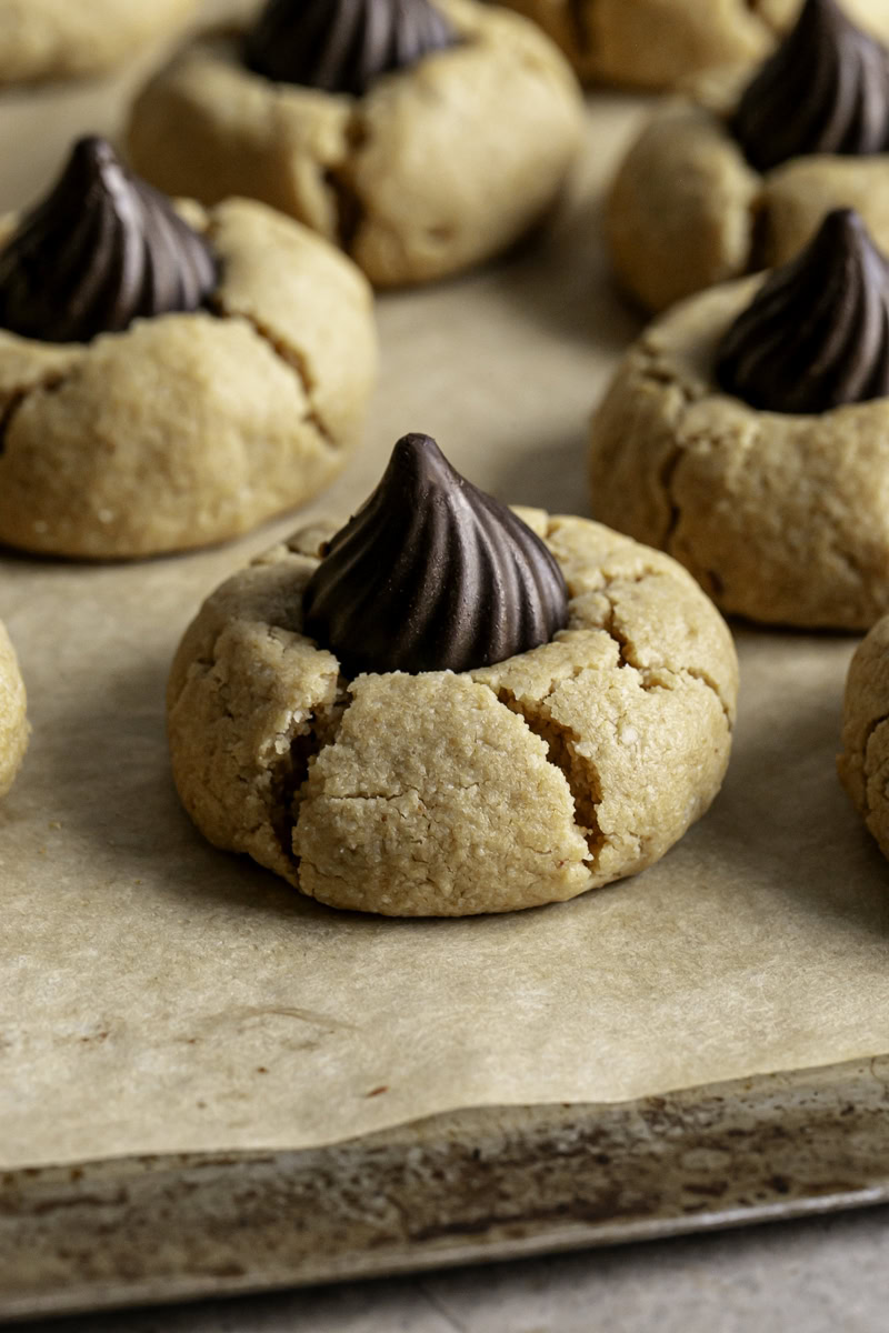 a close up of a Almond Flour Peanut Butter Blossom Cookie on a parchment lined baking sheet.