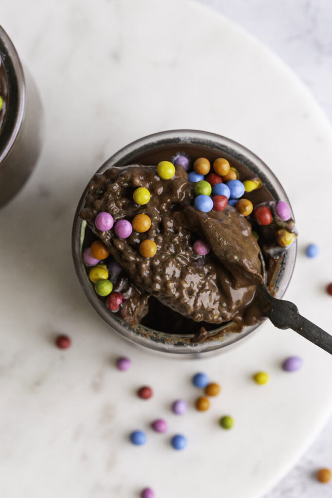 an overhead shot of a jar of Cosmic Brownie Chocolate Chia Seed Pudding with a spoon scooping some out of the jar resting on the mouth of the jar.