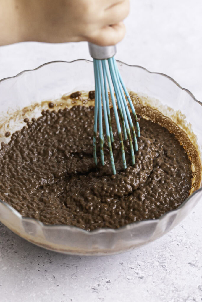 action shot of whisking the chocolate chia pudding in a glass bowl as it has thickened.