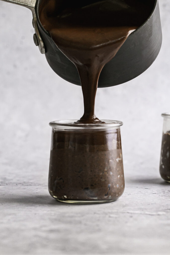 action shot of pouring the chocolate ganache on top of the chocolate chia seed pudding in the jar.