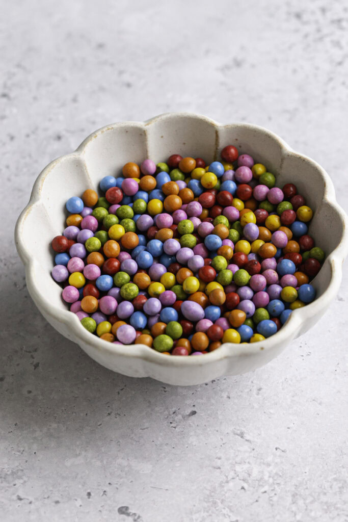 a 3/4 photo of a small bowl filled with rainbow candy coated chocolate chips.