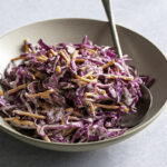 3/4 shot of red cabbage coleslaw in a bowl with a spoon in it.