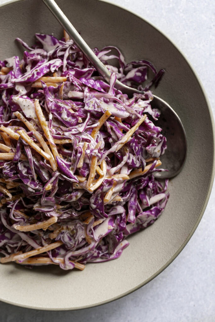 a close up overhead photo of red cabbage coleslaw in a bowl with a spoon sticking out.