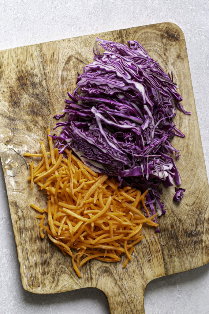 shredded red cabbage and shredded carrots on a wooden cutting board.
