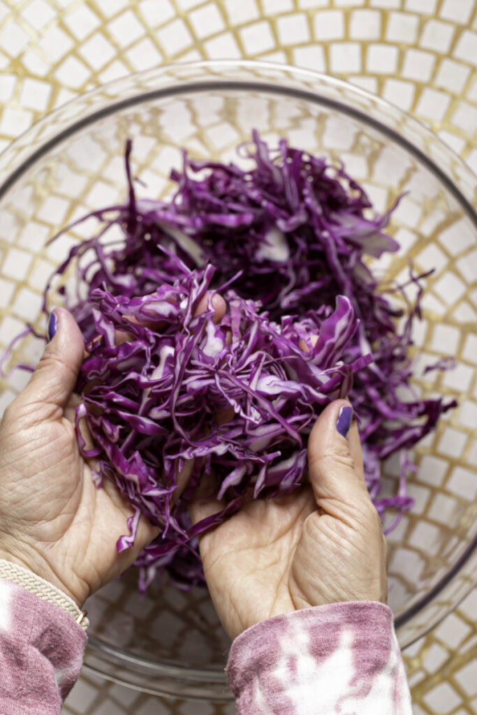 hands lifting shredded cabbage out of a glass bowl.