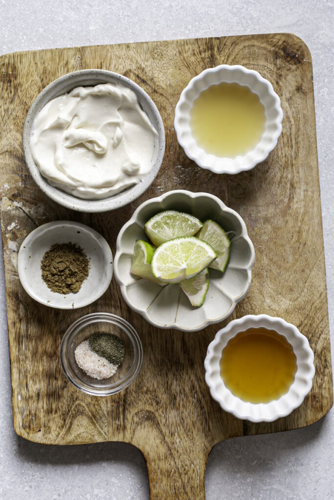 all of the coleslaw dressing ingredients in small bowls on top of a wooden cutting board.