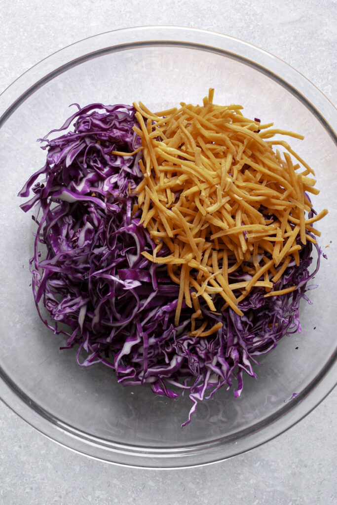 shredded red cabbage and shredded carrots in a large glass bowl.