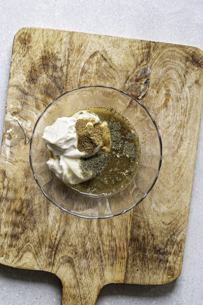 all of the coleslaw dressing ingredients unmixed in a small glass bowl on top of a wooden cutting board.