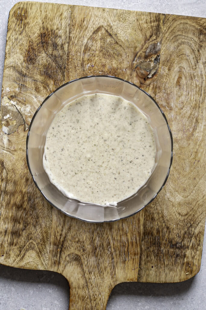 coleslaw dressing in a glass bowl on top of a wooden cutting board.