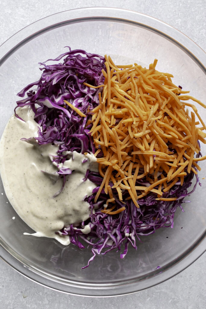unmixed shredded red cabbage and shredded carrots in a large glass bowl with the coleslaw dressing.