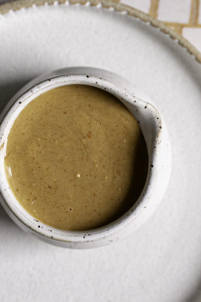 overhead shot of dressing in a ceramic cup on a white ceramic plate.