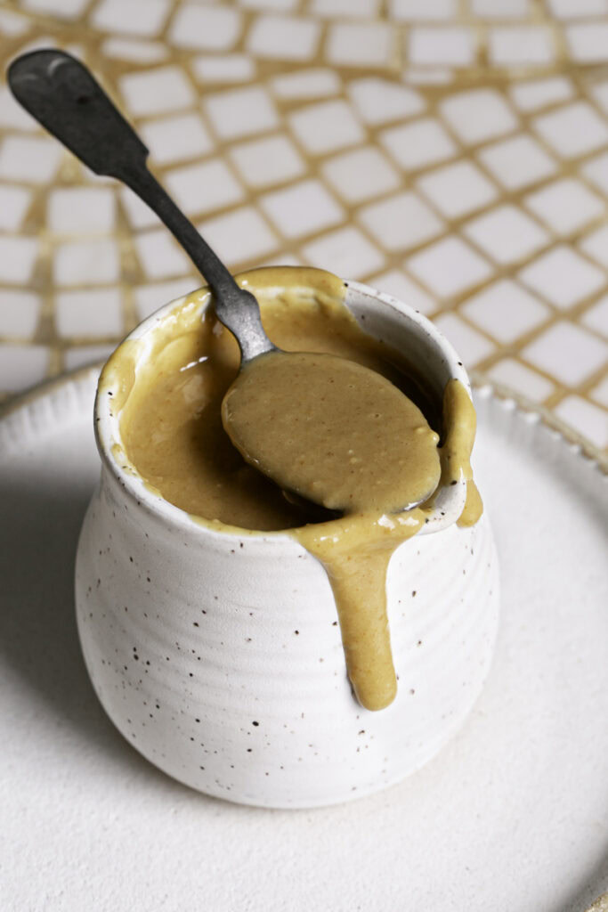 3/4 photo of dressing, some in a spoon resting on the edges of the carafe and dressing dripping down the side.
