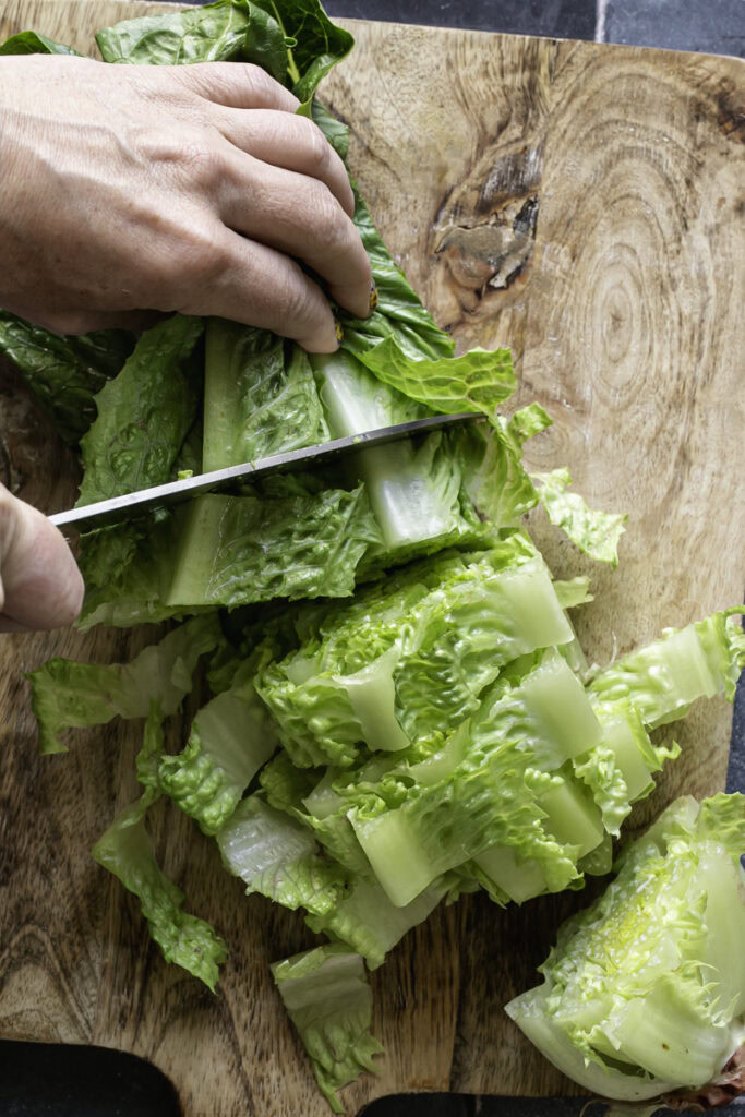 action shot of chopping a head of romaine lettuce on a wooden cutting board.