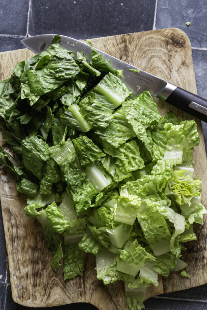 chopped romaine lettuce on a wooden cutting board with a knife.