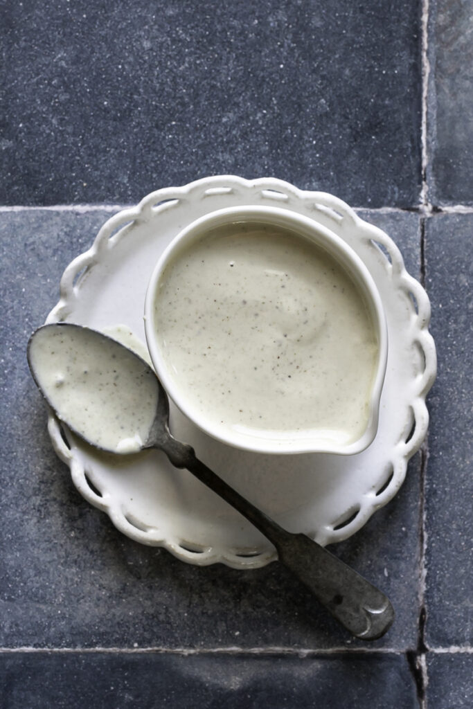 overhead shot of vegan caesar dressing in a bowl on a plate with a spoon beside it with dressing on it.