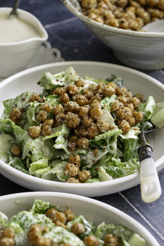close up side view of romaine caesar salad in a bowl topped with crispy chickpea croutons.