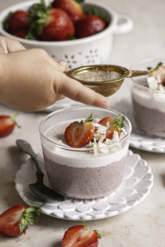 a small hand sifting some freeze dried strawberry powder over the chia seed pudding.