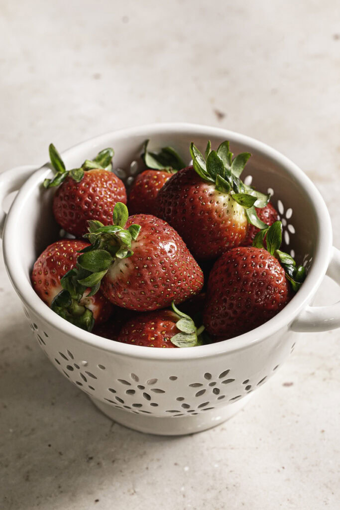 fresh whole strawberries in a small white ceramic berry strainer.