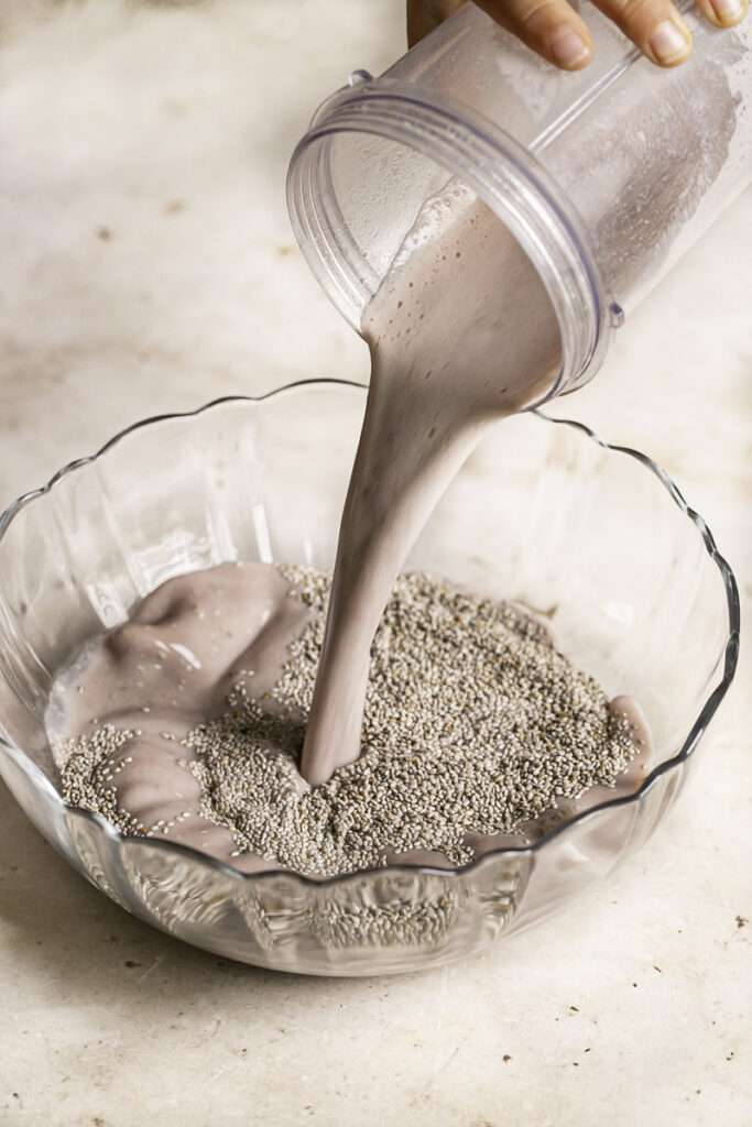 action shot pouring the strawberry hibiscus milk into a glass bowl with white chia seeds.