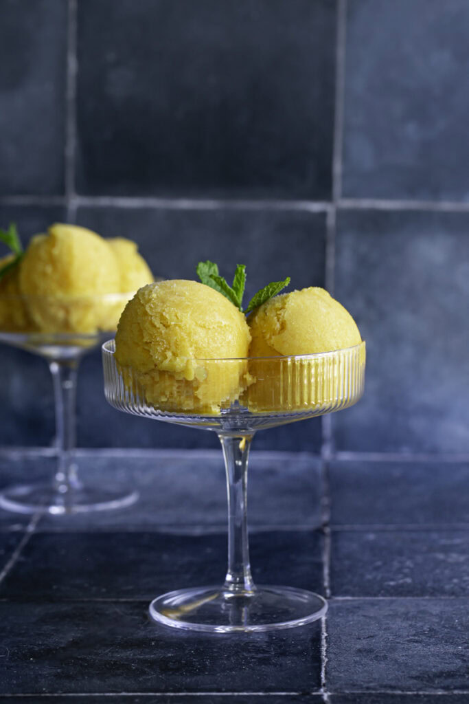 two glasses filled with two scoops of mango peach frozen sorbet garnished with mint leaves.