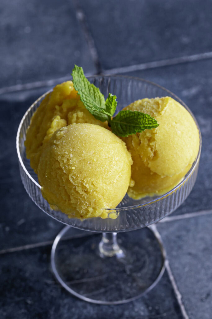 one glass with two scoops of mango peach frozen sorbet garnished with mint.
