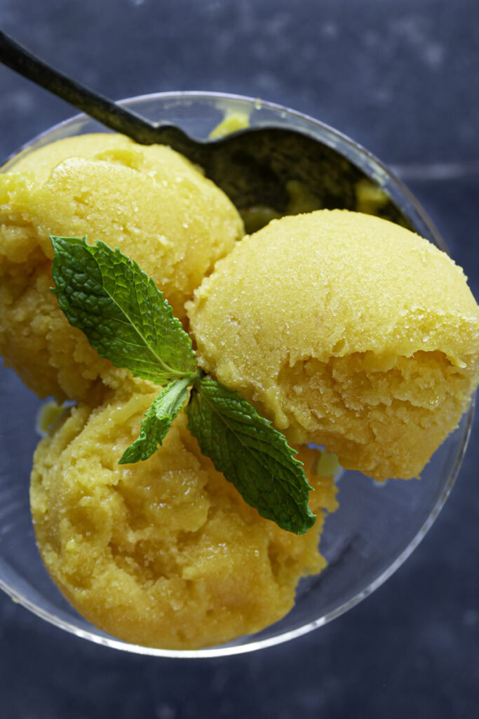 very close up overhead shot of a scoop of mango peach sorbet in a glass garnished with mint.