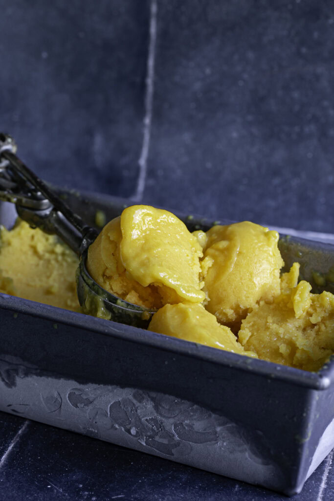 scoops of mango peach sorbet in the loaf pan with an ice cream scoop.
