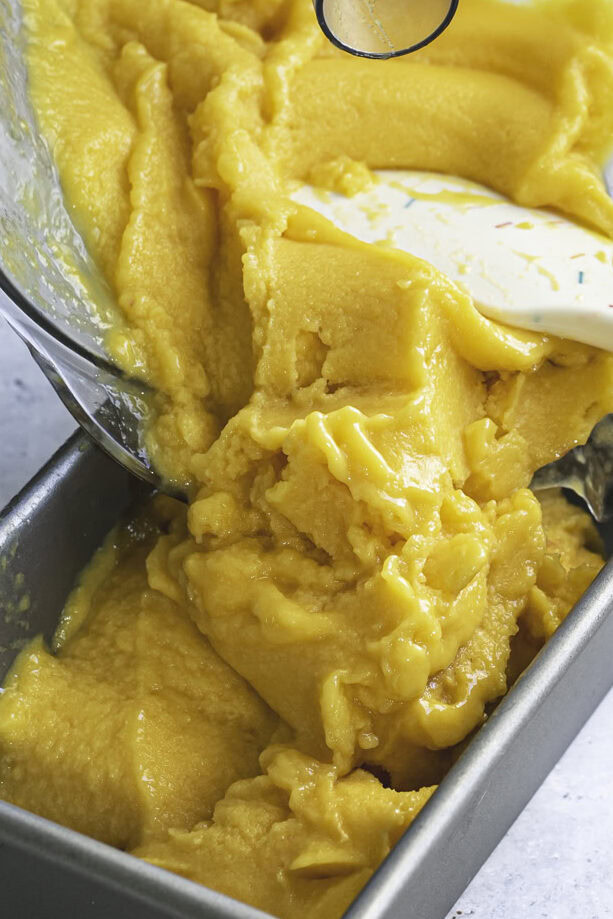 action shot scooping the frozen mango peach sorbet into a loaf pan.