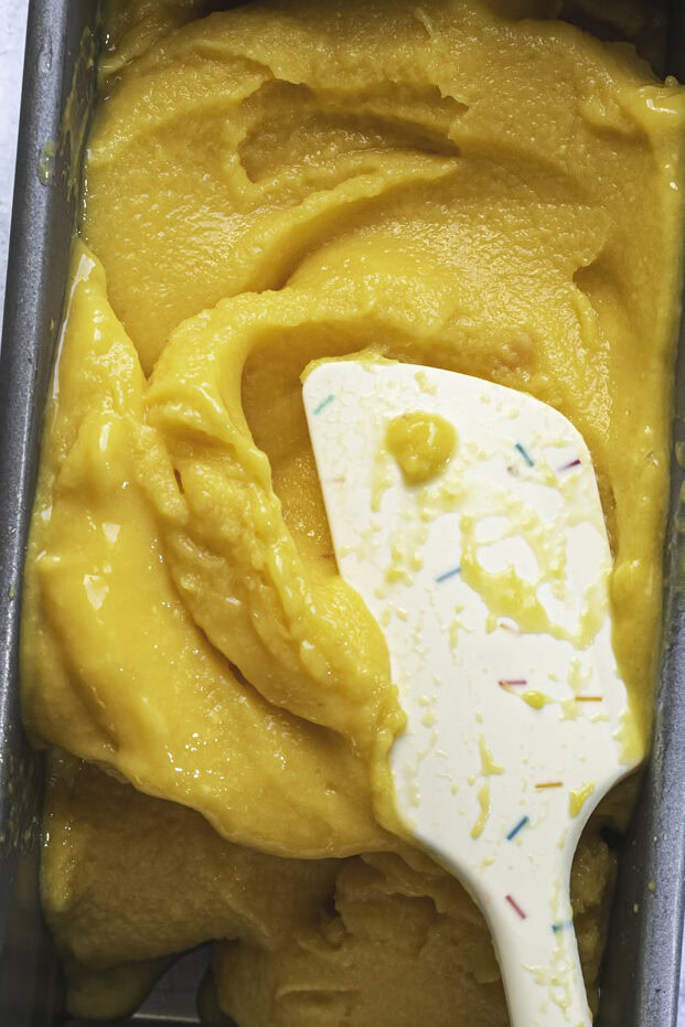 action shot spreading the mango peach sorbet in a loaf pan with a spatula.