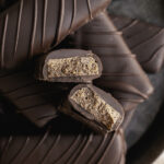 Crispy Peanut Butter Protein Chocolate Candy Bars on an enamel round plate stacked on top of one another, one of the candy bars cut in half to reveal the crispy inside.