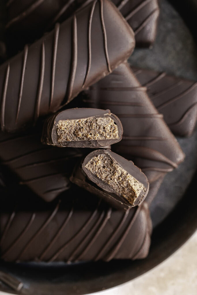 Crispy Peanut Butter Protein Chocolate Candy Bars on an enamel round plate stacked on top of one another, one of the candy bars cut in half to reveal the crispy inside.