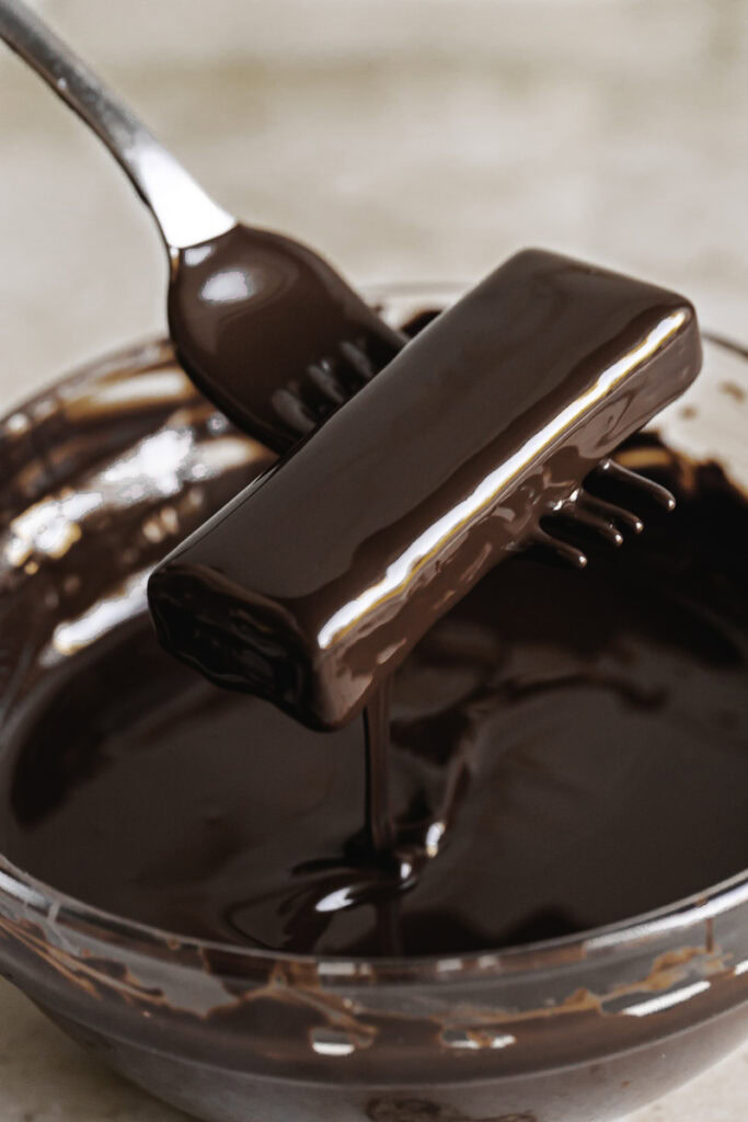 an action shot of a crispy peanut butter protein bar being coated in melted chocolate.