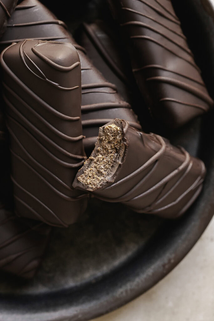 close up of Crispy Peanut Butter Protein Chocolate Candy Bars stacked on a round enamel plate, one of the bars with a bite taken out of it.