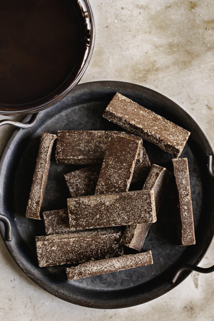 a plate of crispy peanut butter protein candy bar filling before being coated in chocolate with a bowl of melted chocolate above it.