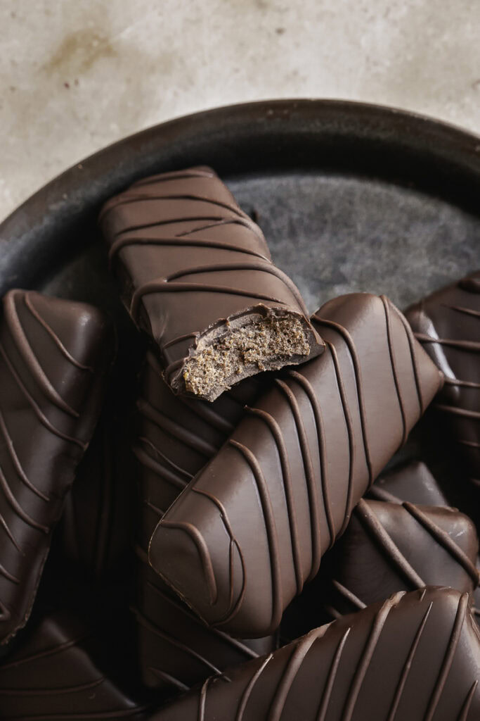 close up of Crispy Peanut Butter Protein Chocolate Candy Bars stacked on a round enamel plate, one of the bars with a bite taken out of it.