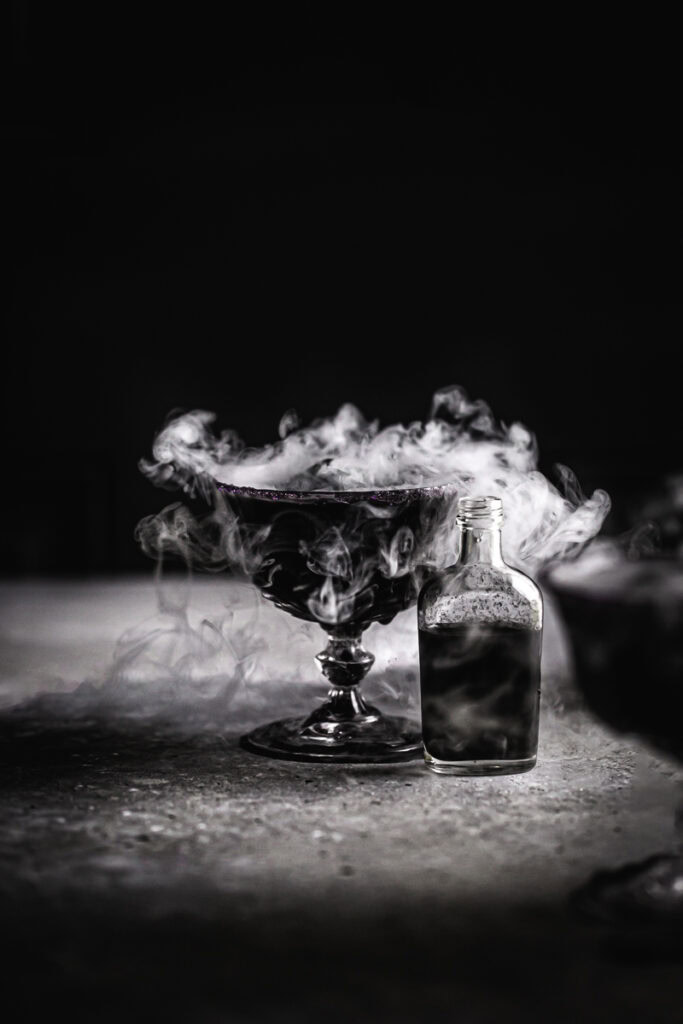 a black apple juice mocktail with dry ice smoking out of the glass.