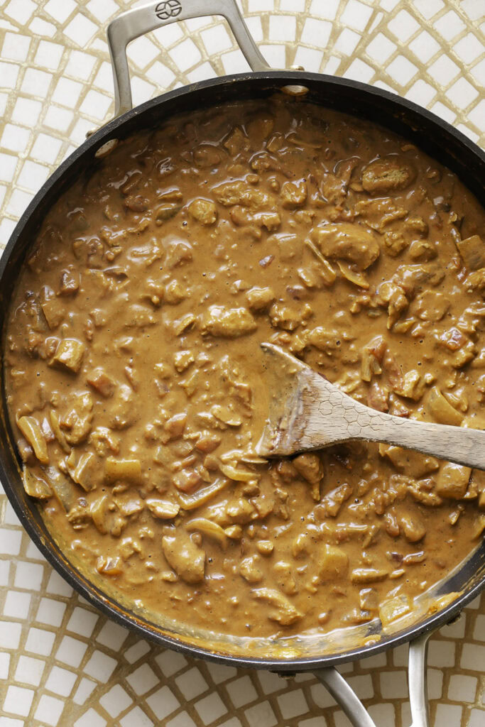 indian butter chicken sauce in a skillet with a wooden spoon.