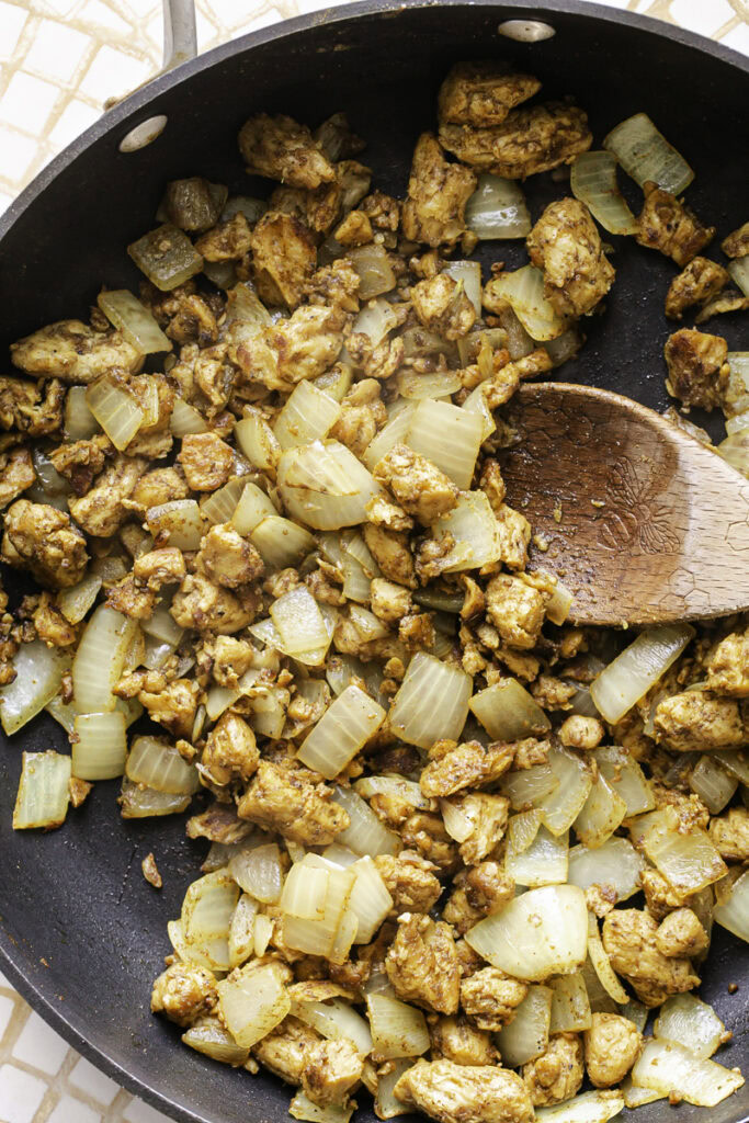 plant-based chicken and sauteed onions in a skillet with a wooden spoon.