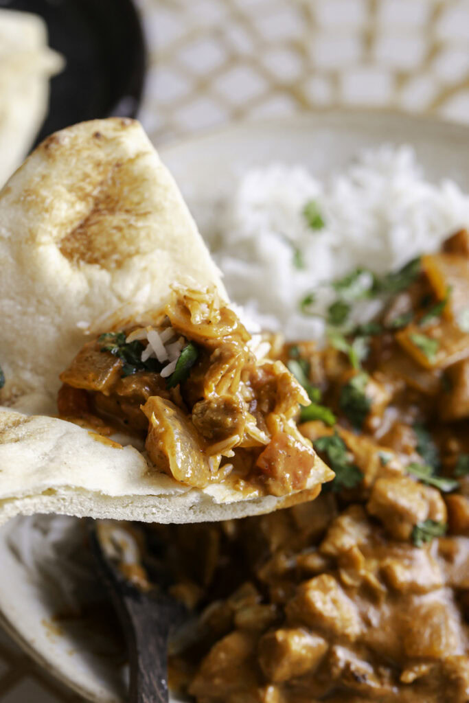 action shot of scooping indian butter chicken on a piece of naan bread.