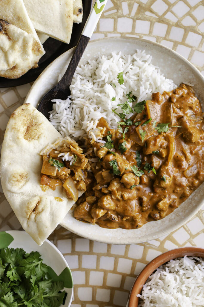 overhead shot of indian butter chicken in a bowl with rice and a piece of naan bread.