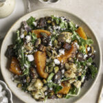 Roasted Butternut Squash Fall Harvest Salad with a jar of creamy apple cider vinaigrette, a bowl of pistachios, and a bowl of vegan feta cheese.