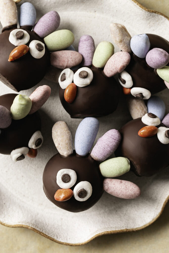 overhead shot of no-bake date almond flour brownie bite turkeys with pastel colored almond feathers, googly eyes and a candy beak on a plate.