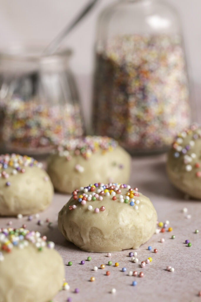 Buttery Soft Italian Sprinkle Biscotti Cookies with sprinkles around it and 2 jars of sprinkles in the background.