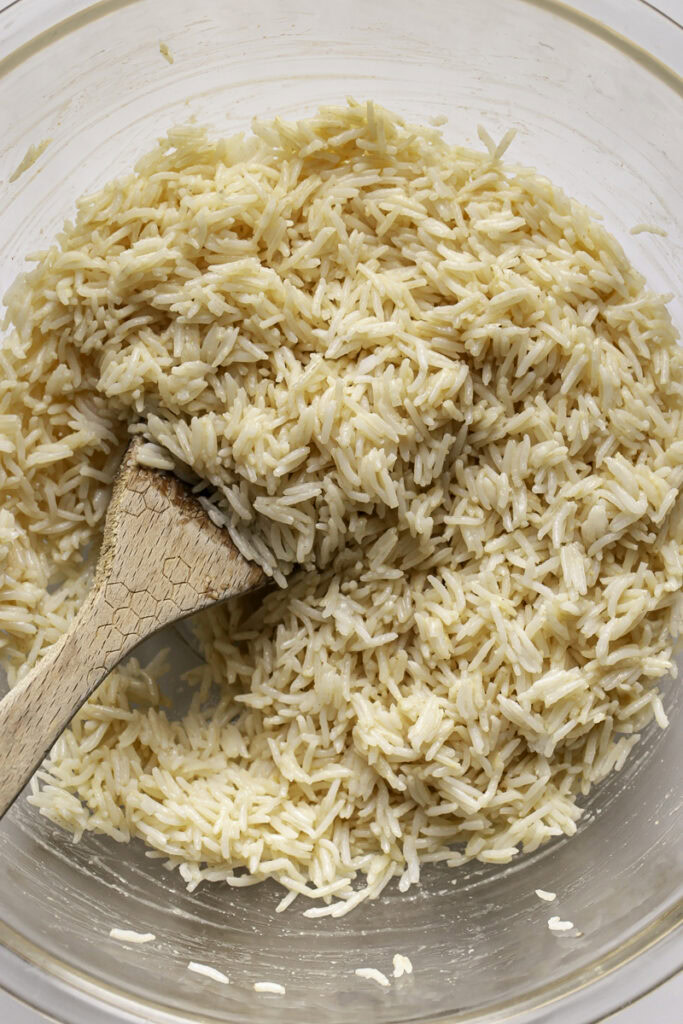 cooked rice in a bowl with a wooden spoon tossed with dressing.